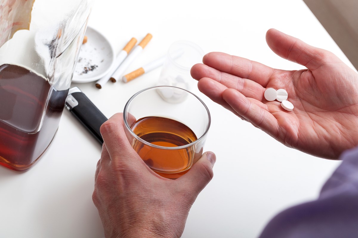 Alcohol, smoking and medication. A man holds a glass of brown alcohol and medication in his right hand. As the most common causes of chronic pancreatitis