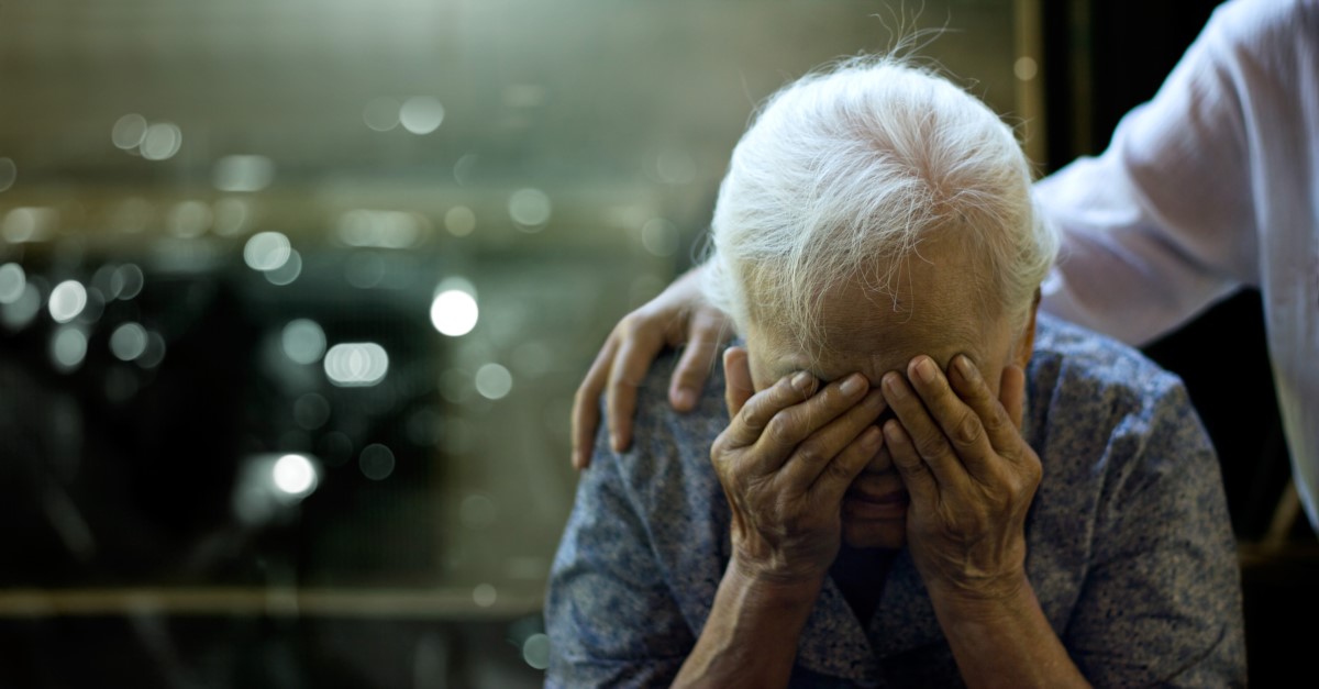 An elderly woman has a health problem, her head is supported by her arms and a person is holding her shoulders