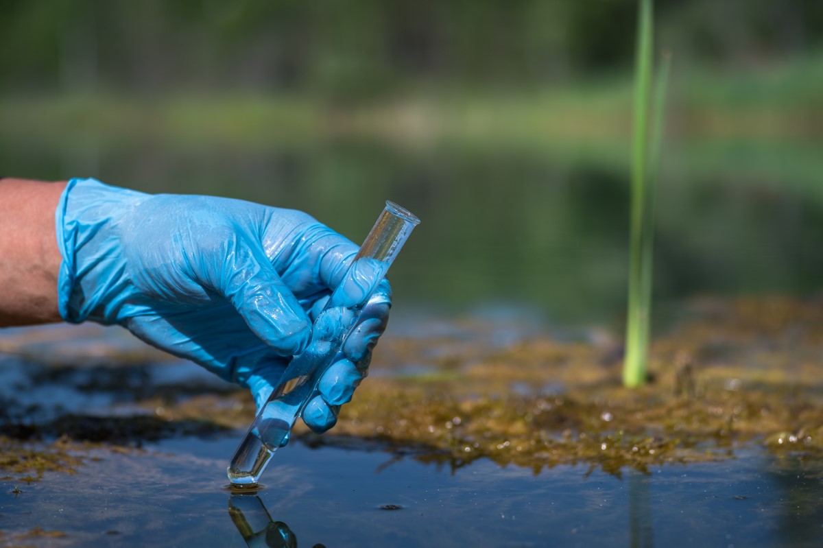 Gloved hand, holding a test tube, taking a water sample