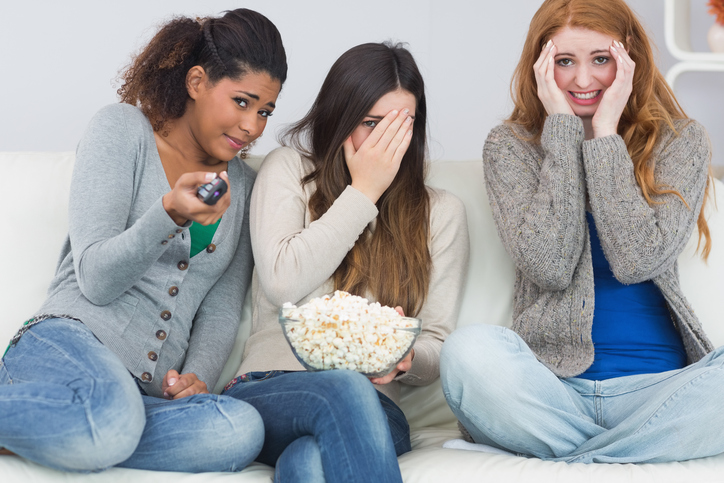 Three girls are scared, watching a scary movie, popcorn in a bowl