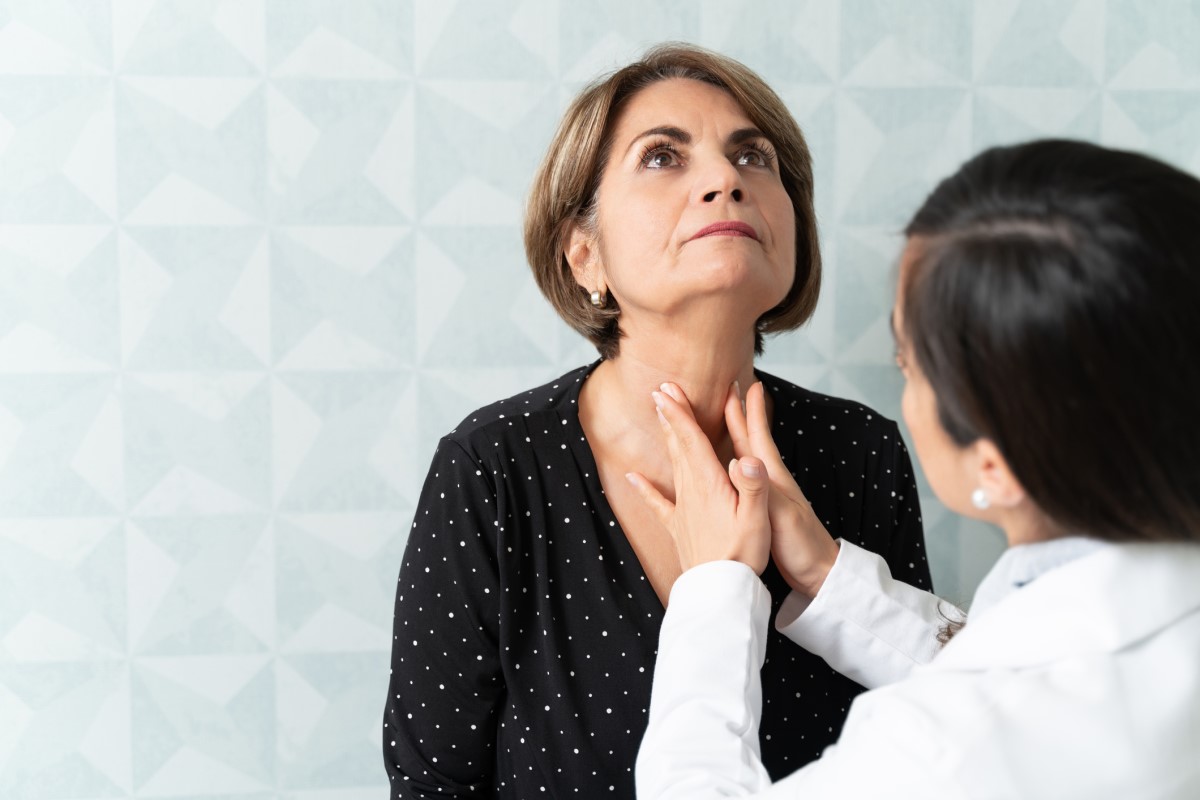 Doctor palpating thyroid gland, elderly woman sitting opposite