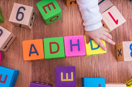 children's letter cubes, arranged to form the name ADHD, with the child's hand