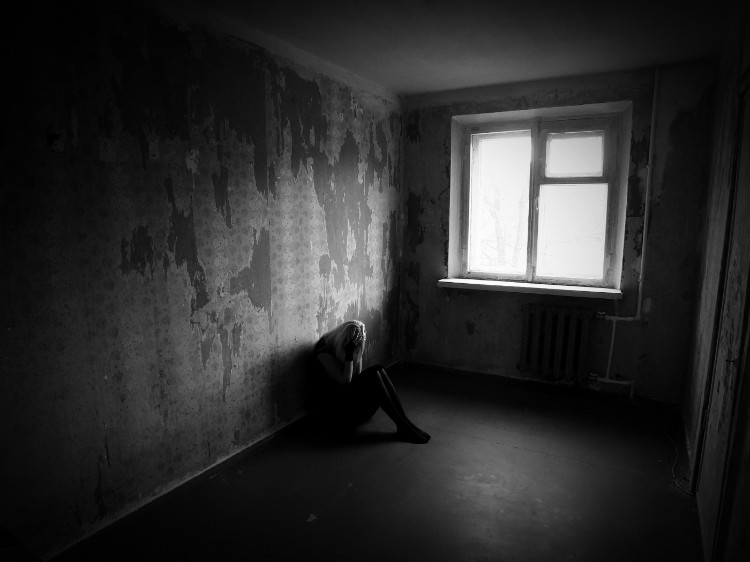 a woman sitting in a dark room leaning against the wall, holding her face with her hands
