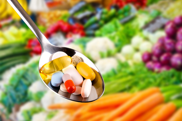 vitamins in tablets on a spoon, lots of fresh vegetables in the background