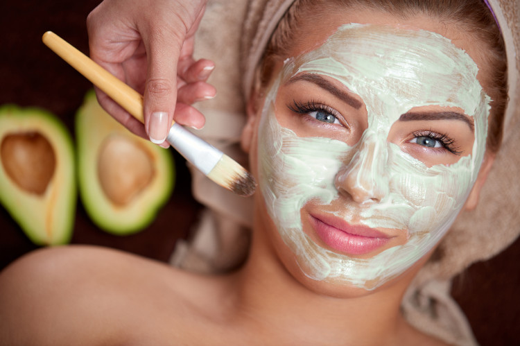 woman with a turban on her head and a green natural mask on her face, in the background is a cut avocado