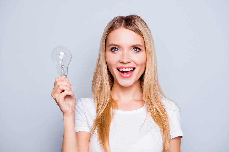 laughing woman with blonde hair in a white T-shirt holding a light bulb