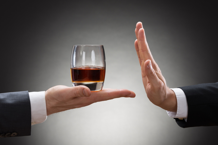 a person's hand is holding a glass of alcohol and another person's hand is rejecting it