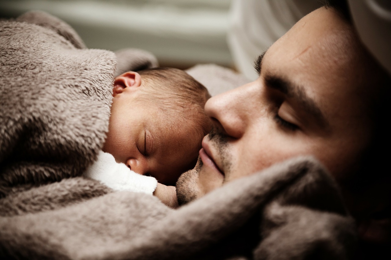 the baby sleeps next to his father under a brown blanket