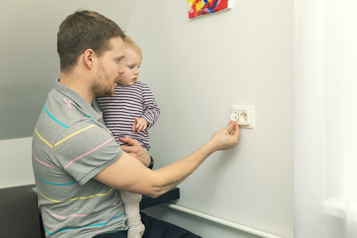 Dad holds a small child in his arms and closes the plug with an electrical plug