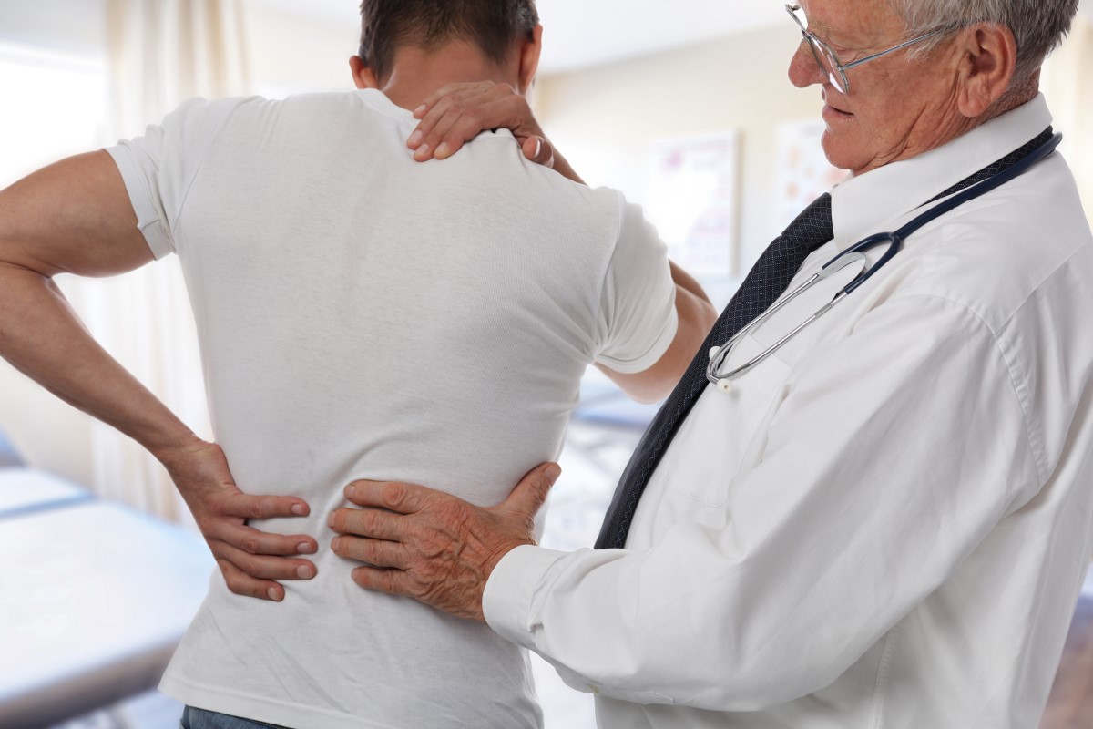 Back pain, doctor examines young man, his back hurts