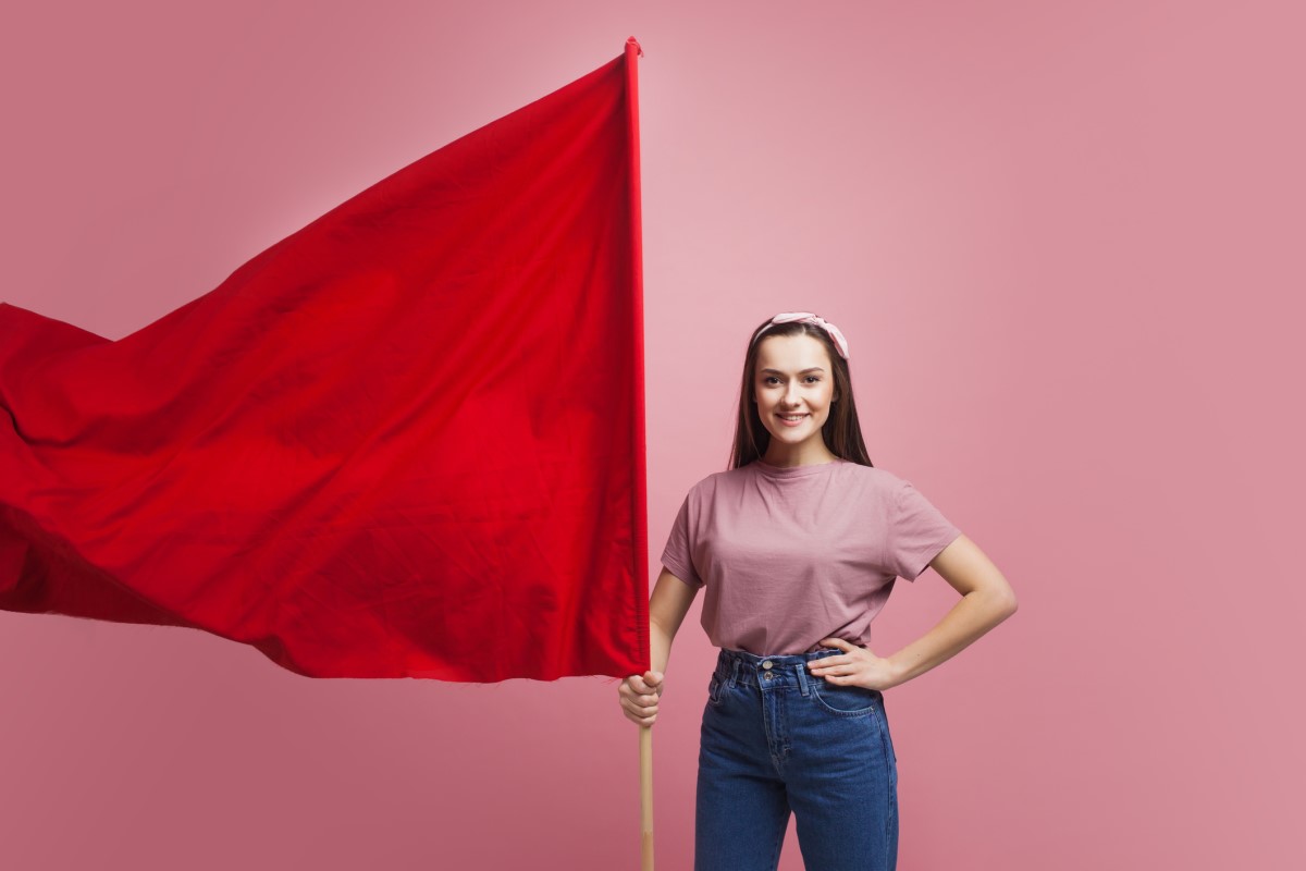 A woman is holding a large red flag as a warning.