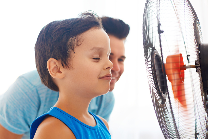 A boy and his dad standing in front of a fan