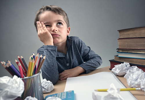 a schoolboy sitting at his desk, thinking about something, with a notebook, paper, pencils on his desk