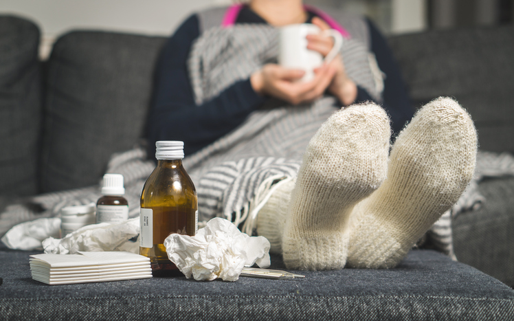 a sick woman is lying in bed with warm socks and pills and syrups beside her