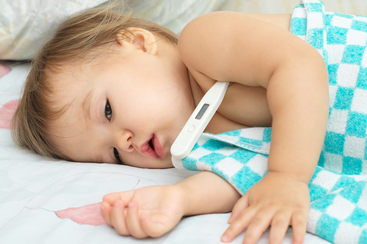 Lying child covered with a thin blanket with a thermometer.