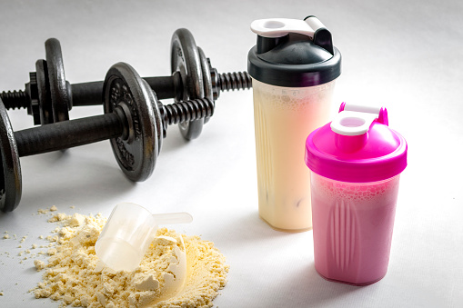 Two one-handed dumbbells. They're placed next to the protein drinks in two bowls. There's a protein powder with a measuring spoon next to them.