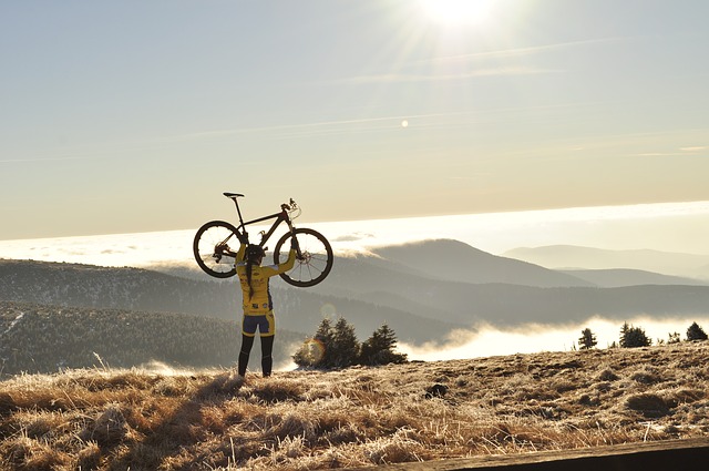 A cyclist lifts her bicycle above her head. In the background are mountains in the fog.