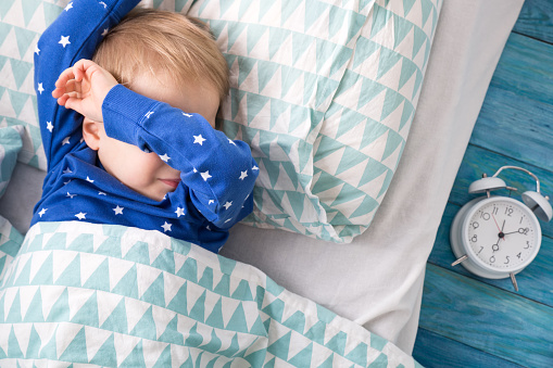 Waking up little boy in blue pyjamas, next to the alarm clock