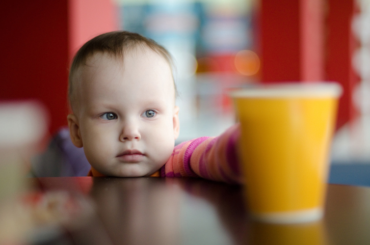 A small child reaches for a glass of water on the table