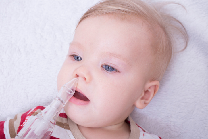 suctioning snot from the child's nose with a suction pump