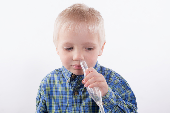 The boy is holding a mucus extractor to his nose