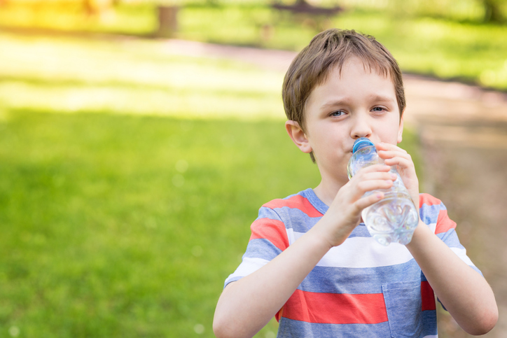 Boy drinking water from bottle, green grass in background