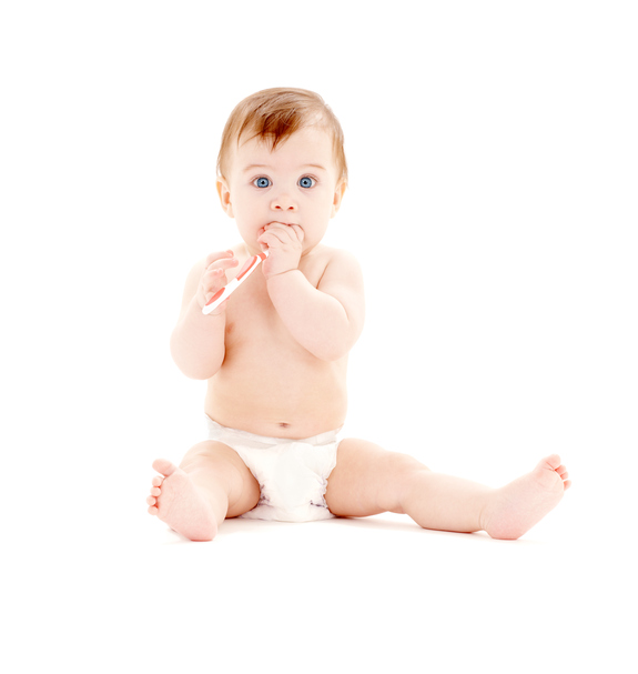 A small child in a diaper is sitting up, with a toothbrush in his hands, which is in his mouth
