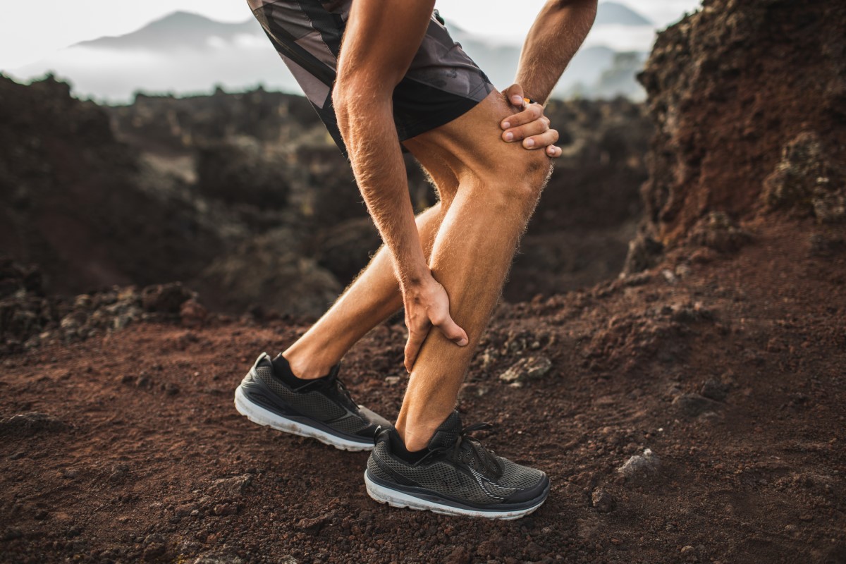 Muscle cramp - a man, athlete, hiker, holds his sore leg in the shin area.