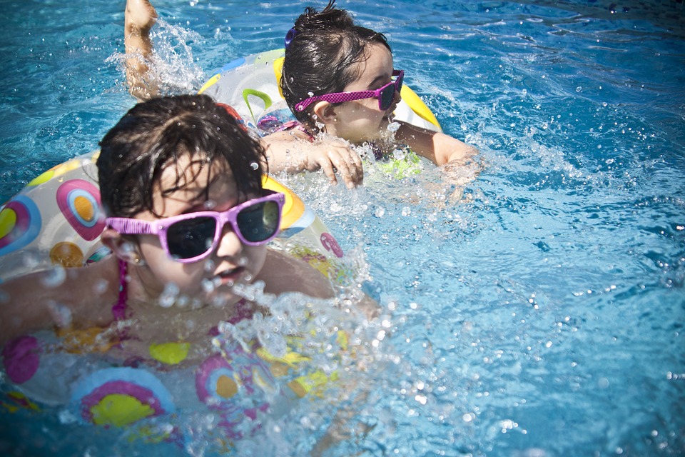 Two kids are swimming in the water. They're wearing sunglasses with pink frames. They're in floating bikes.