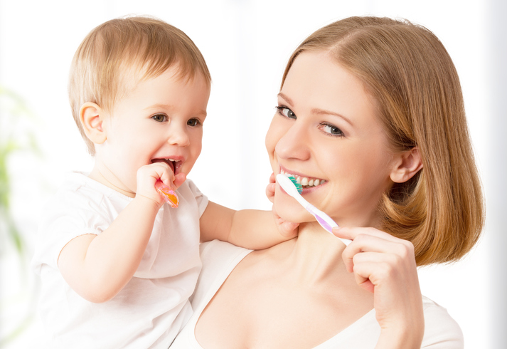 A mother brushes her teeth with her child in her arms.