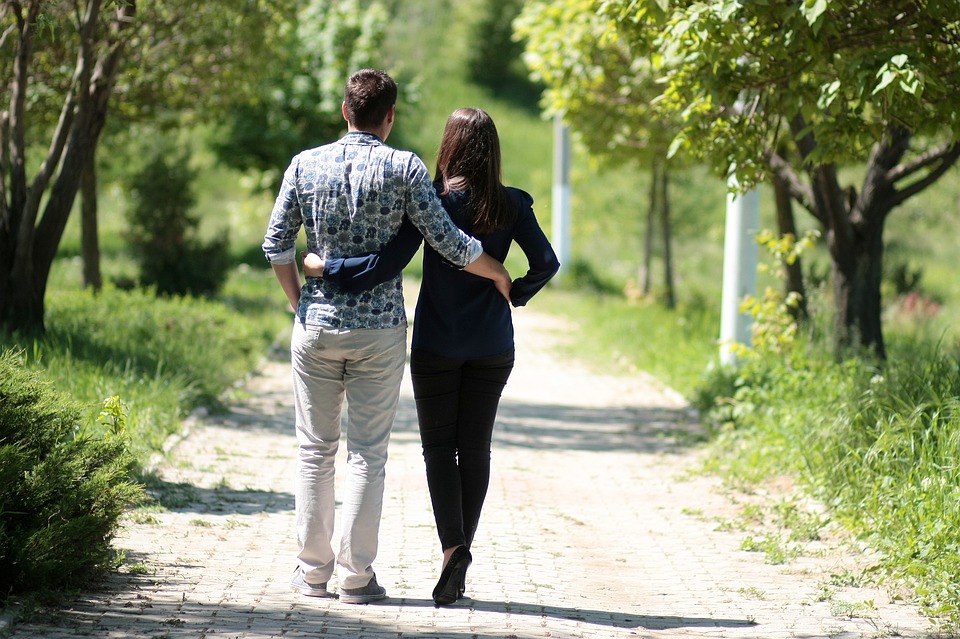 Couple walking on a nature trail. Holding each other around the waist. Green trees. Green grass.