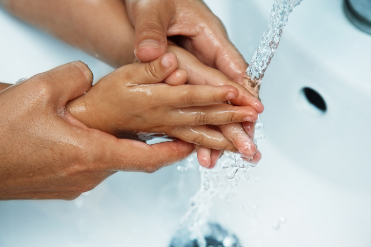 mother's hands over the sink washing baby's hands under running water