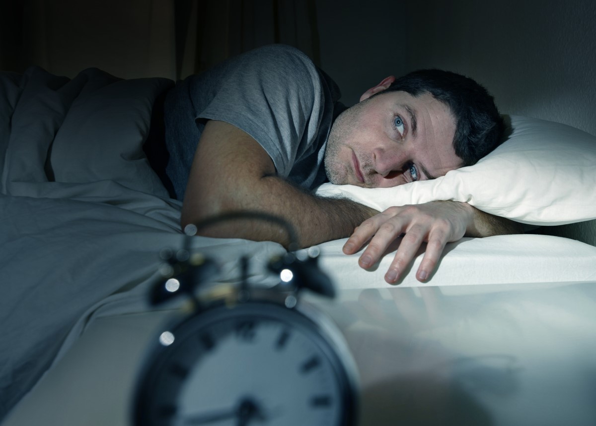 Sleep disturbances, man lying in bed late at night and unable to fall asleep, clock on table