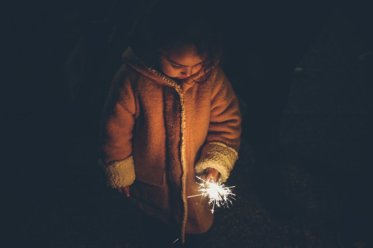 a little girl in a coat and with a sparkler in her hand looking sadly at the ground