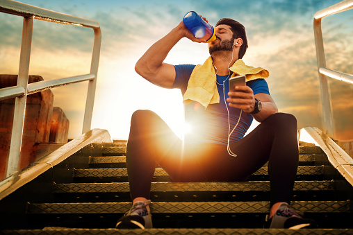 An athlete sitting on the stairs. Sunset. Drinking a nutritional supplement from a jar.