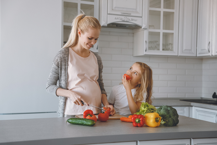 Pregnant mother and daughter prepare a healthy meal in the kitchen.