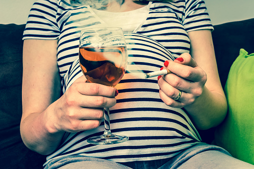 Pregnant woman in a striped T-shirt with a cigarette and a glass of wine