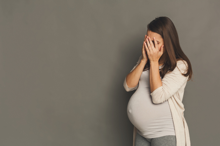 A tired pregnant woman, covering her face with her hands.