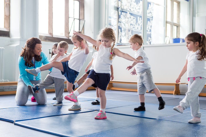 Young children in the gym, practicing with the teacher.