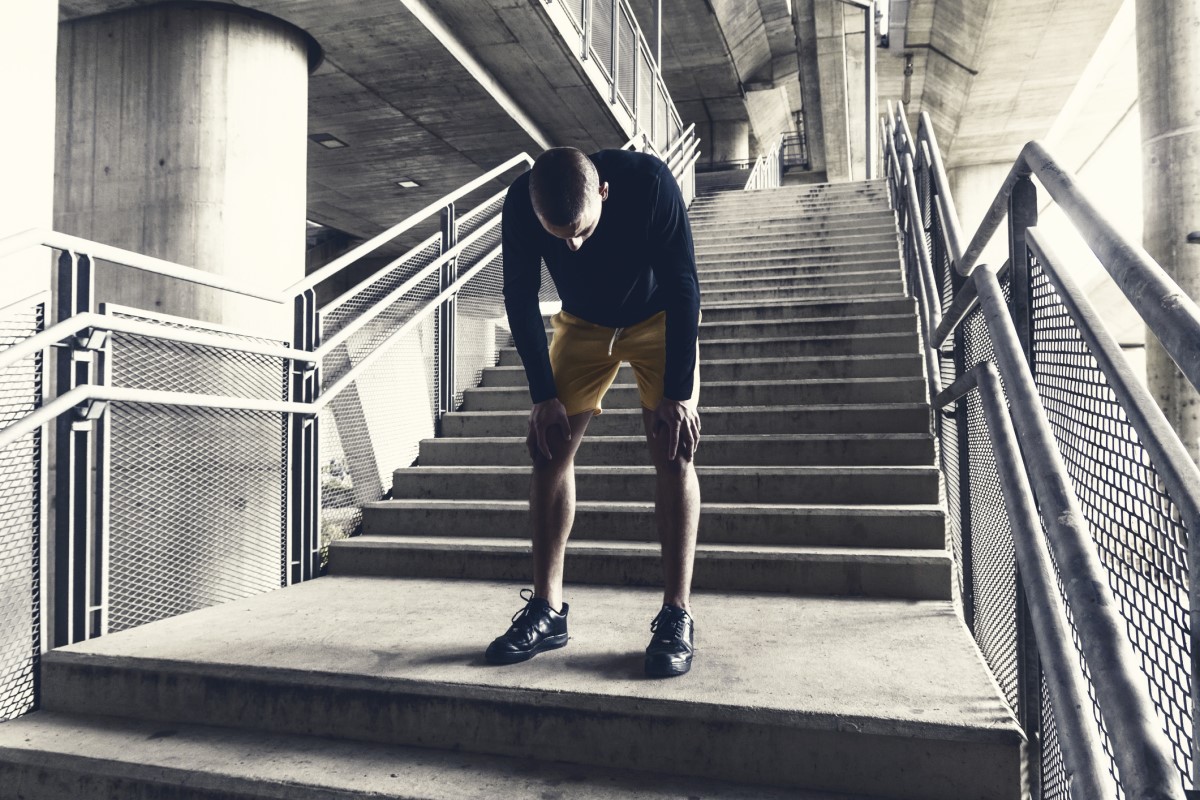 A tired runner, a man, rests under the stairs after a workout.