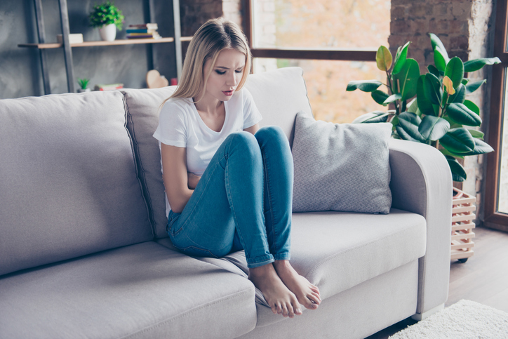 the woman is in pain sitting on the sofa 