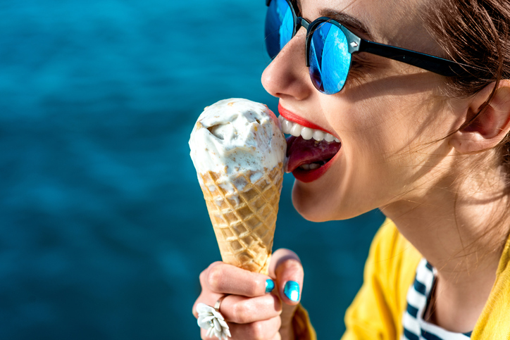 woman in sunglasses licking ice cream next to the water