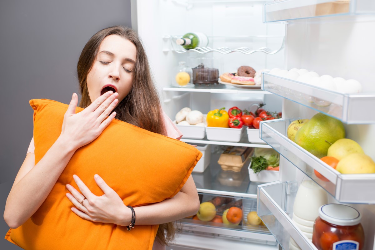 A woman sleeping next to a refrigerator, illustrating eating habits as a factor influencing sleep quality.