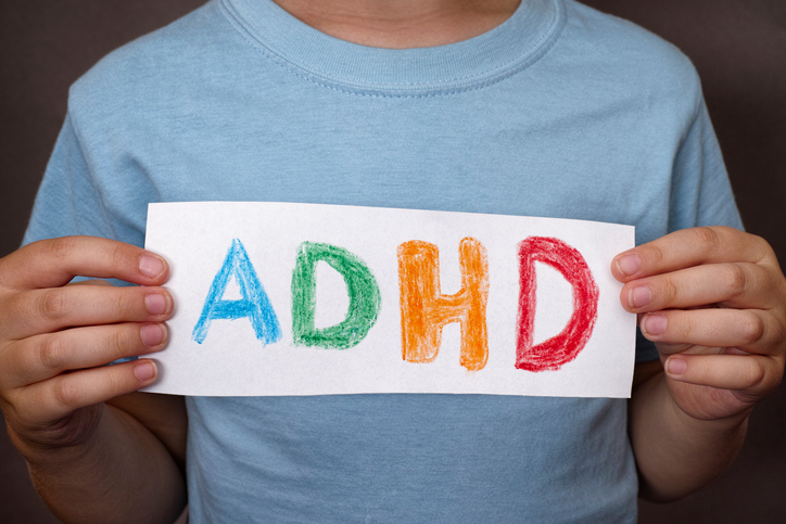 A boy holds a sign with a colourful ADHD sign on it