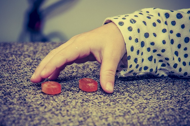 A child's hand, two red candies, bad eating habits