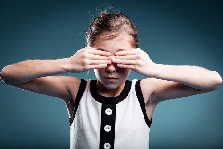 a young girl covers her eyes as a sign of blindness