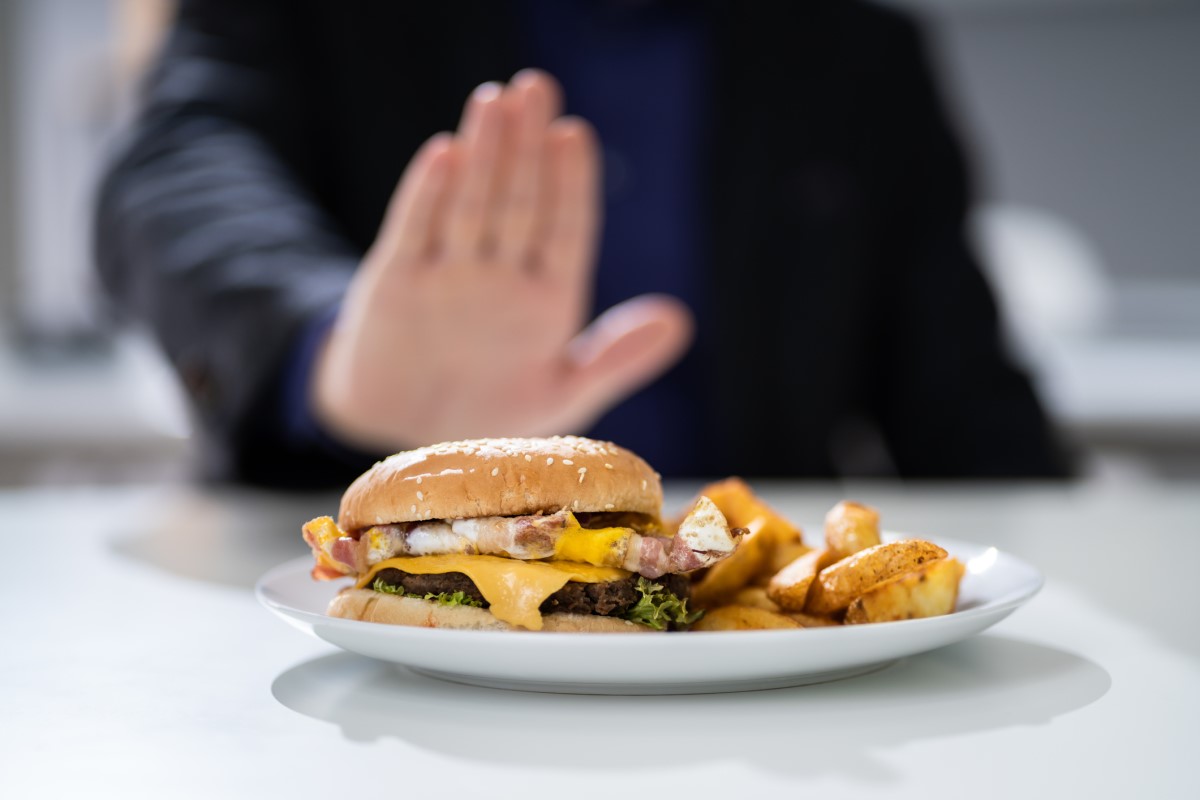 Inappropriate food as a cause of heartburn - a hamburger on a plate that a man is refusing.