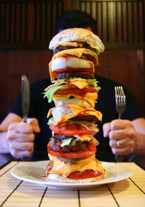 A man sits at a table, a tall hamburger on his plate, a jumbo meal