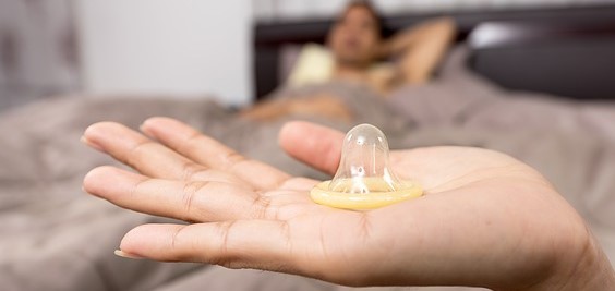 condom on woman's hand, man lying in bed