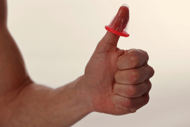 A man holds a condom on his finger (thumb) as a symbol of protection against sexually transmitted diseases and against fertilization of the egg by sperm